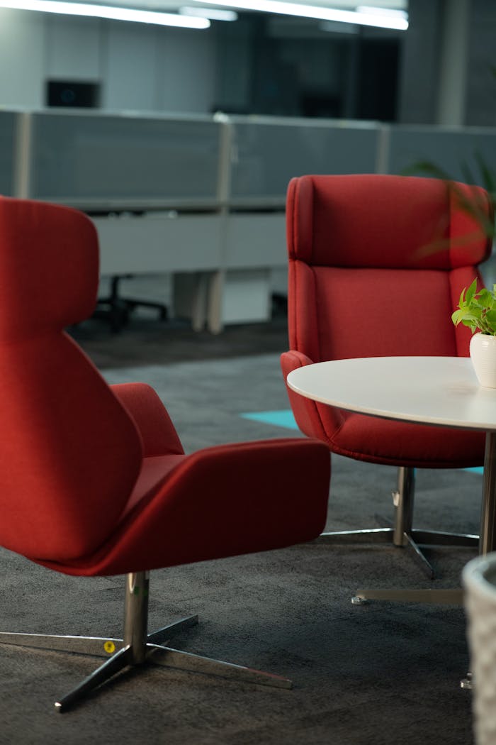 Contemporary office lounge featuring stylish red chairs and a round table, perfect for meetings.